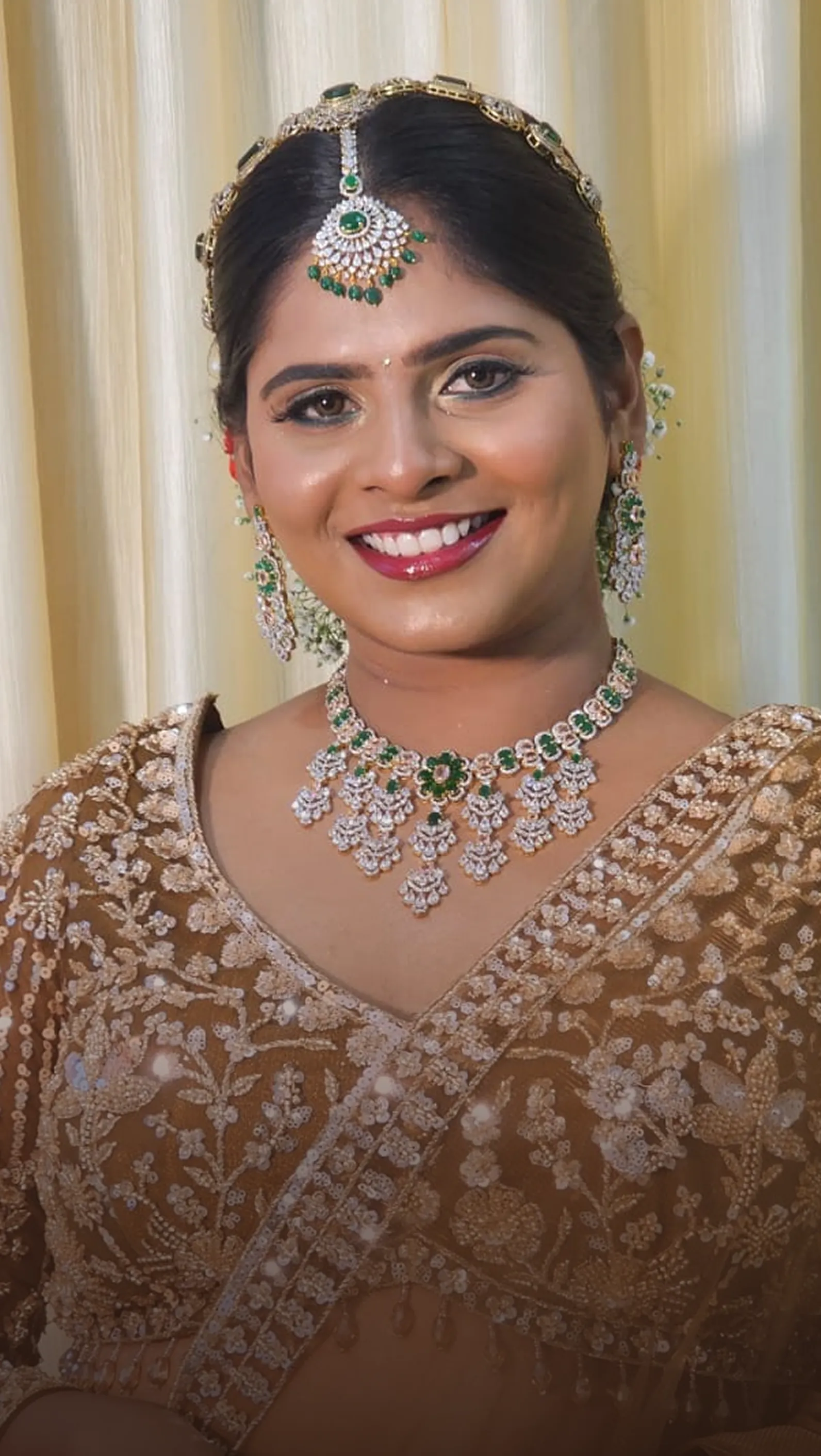 Smiling bride in a gold lehenga with an emerald necklace