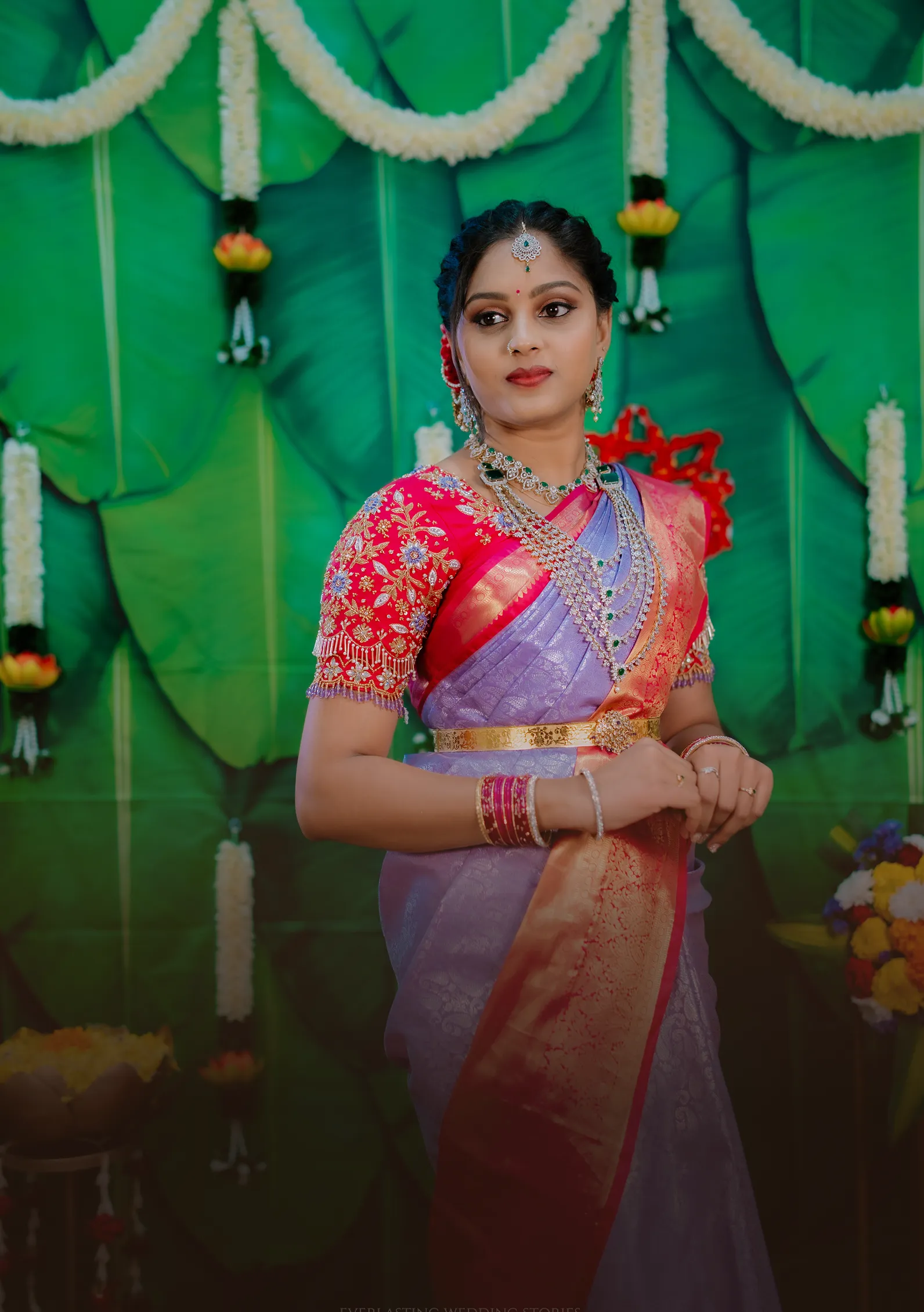 Bride in a lavender and red saree against banana leaves